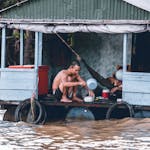 A man sits on a flooded wooden houseboat during a heavy flood.
