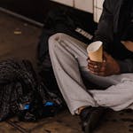 Close-up of a man sitting on a city street holding a paper cup, highlighting urban life challenges.