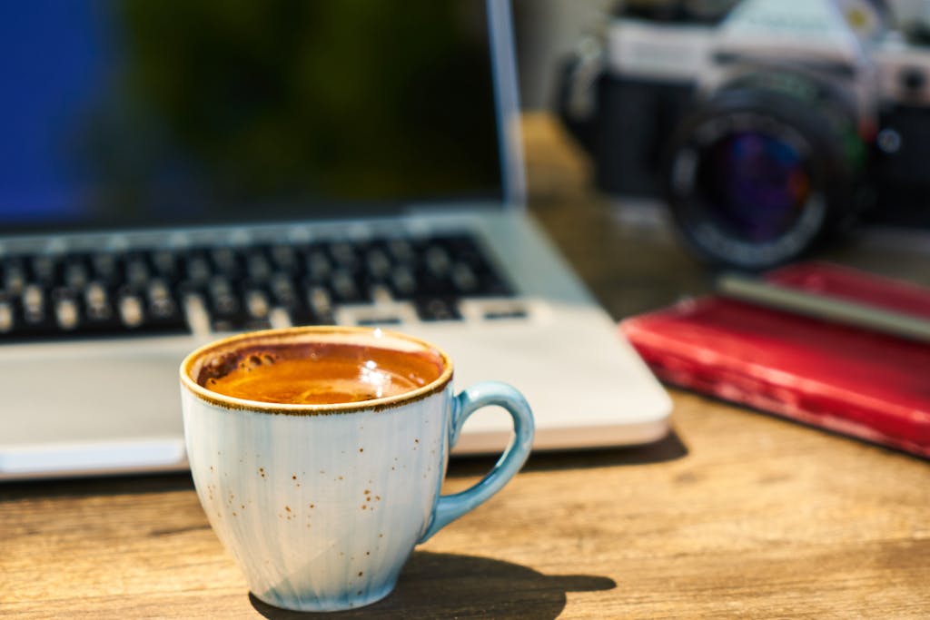 Press Release A cozy workspace with a cappuccino, laptop, and vintage camera on a wooden desk.