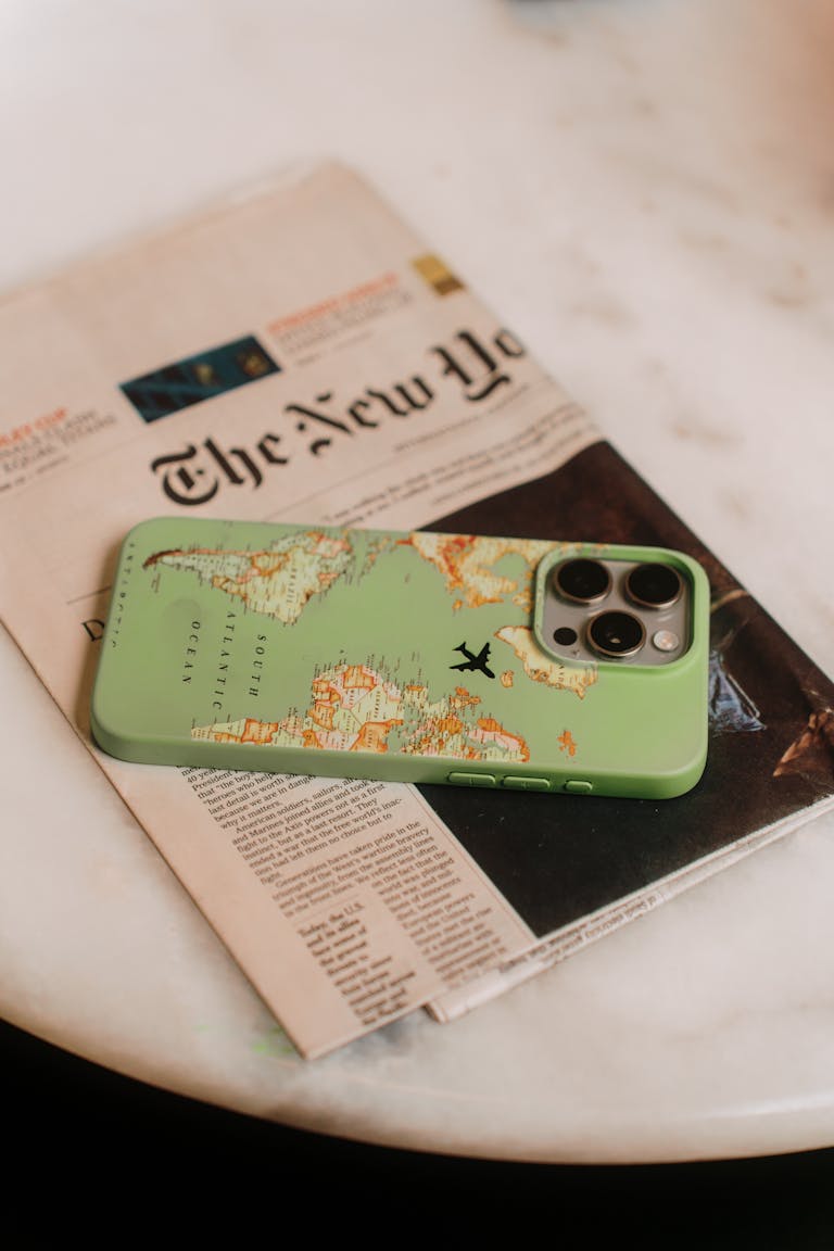 IPS Latest with a map-themed case sits on a tabletop beside a newspaper, emphasizing travel and technology.