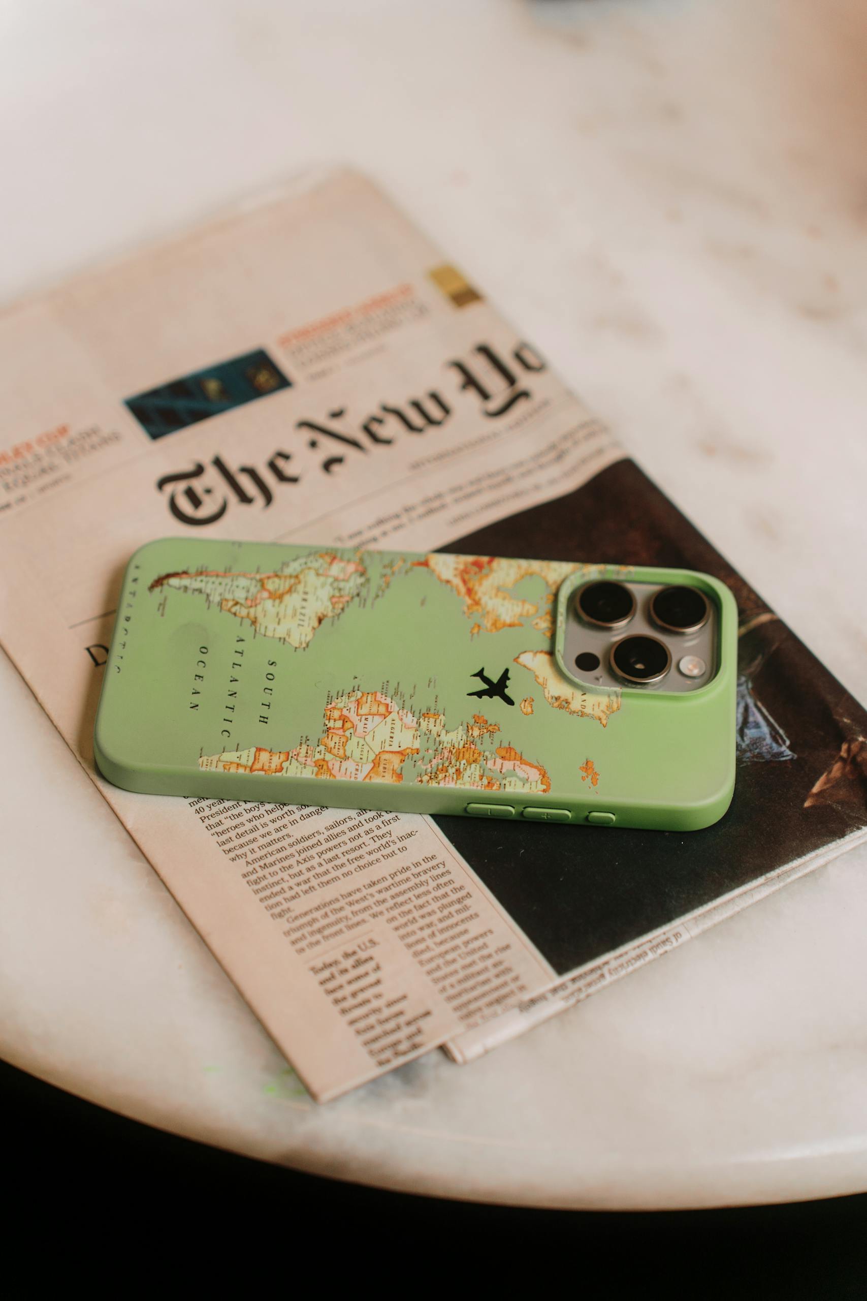 IPS Latest with a map-themed case sits on a tabletop beside a newspaper, emphasizing travel and technology.