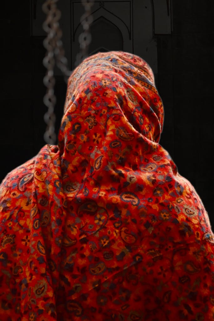 Ravleen Kaur draped in a red patterned shawl with intricate designs, captured from behind in an indoor setting.