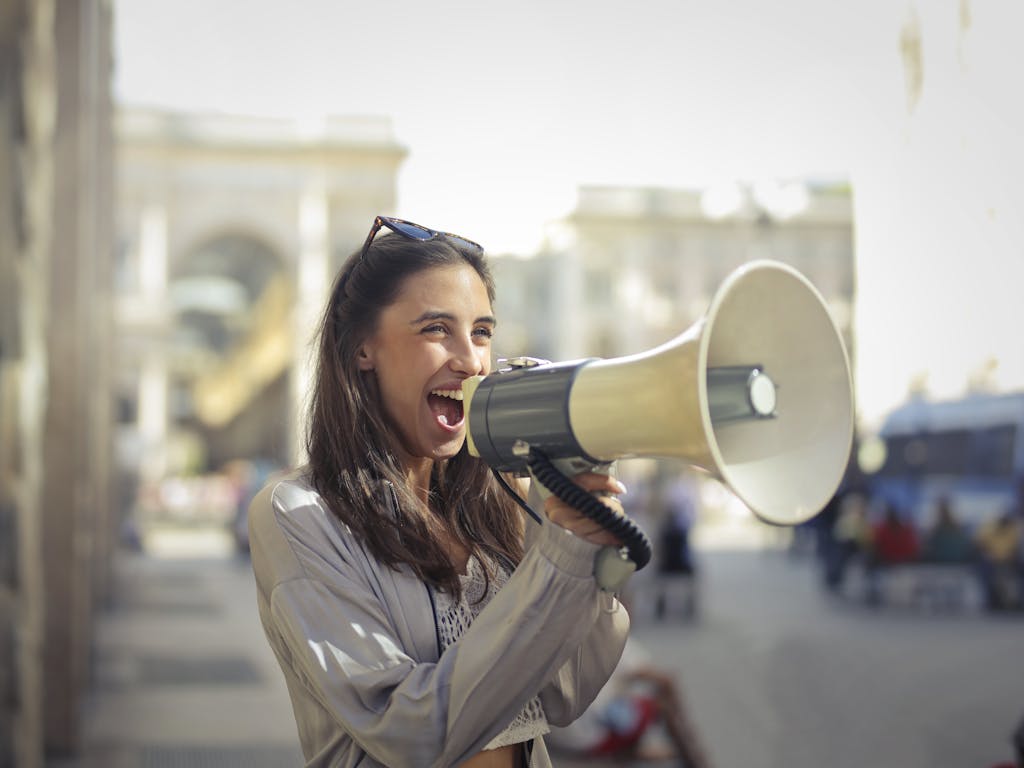 CGTN News Cheerful young woman in a casual outfit shouting into a megaphone on a sunny day.