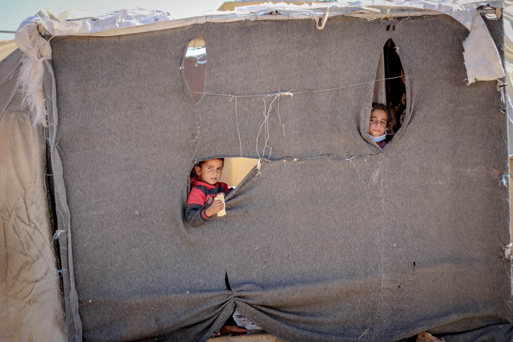 Startup or World War Children peeking through a makeshift tent in Idlib, highlighting resilience and hope.