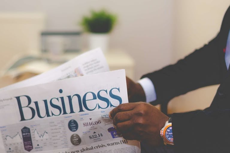 Calmered Latest Jobs News by NewsArena.tech FTAsiaManagement Economy News from FintechAsiaClose-up of a businessman reading a newspaper indoors, focusing on business headlines.