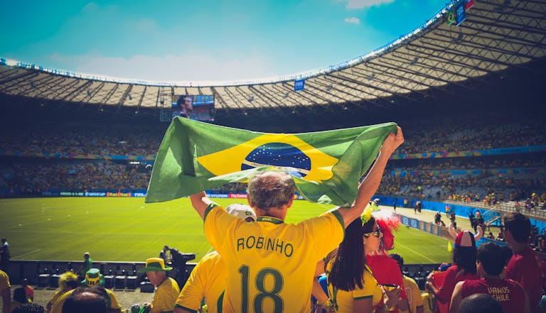 FIFA World Cup 2026 Excited Brazilian fans holding flag at soccer match in vibrant stadium atmosphere.
