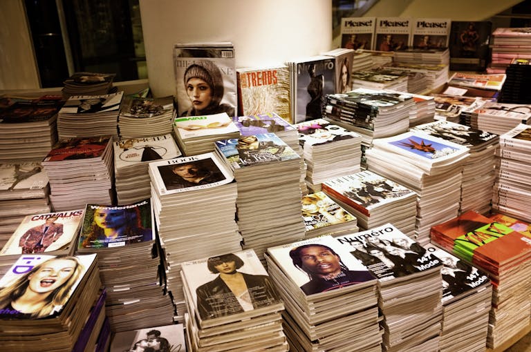 Apna News Rameja My News GH Huge stacks of diverse fashion and lifestyle magazines piled high in an indoor store setting.