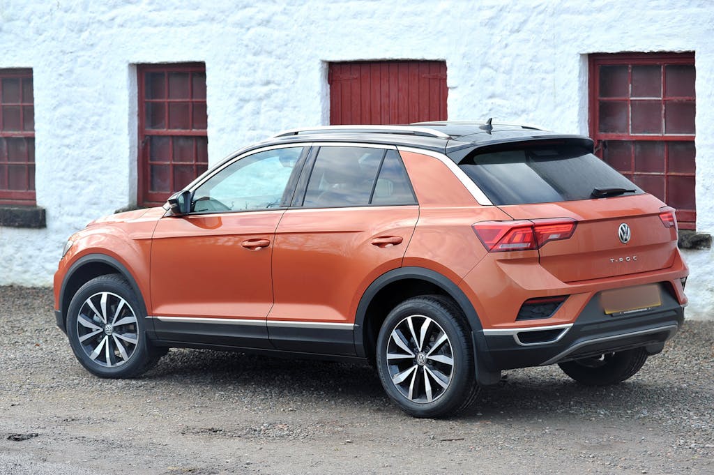 Orange Volkswagen T-Roc SUV parked beside a rustic building with red accents.