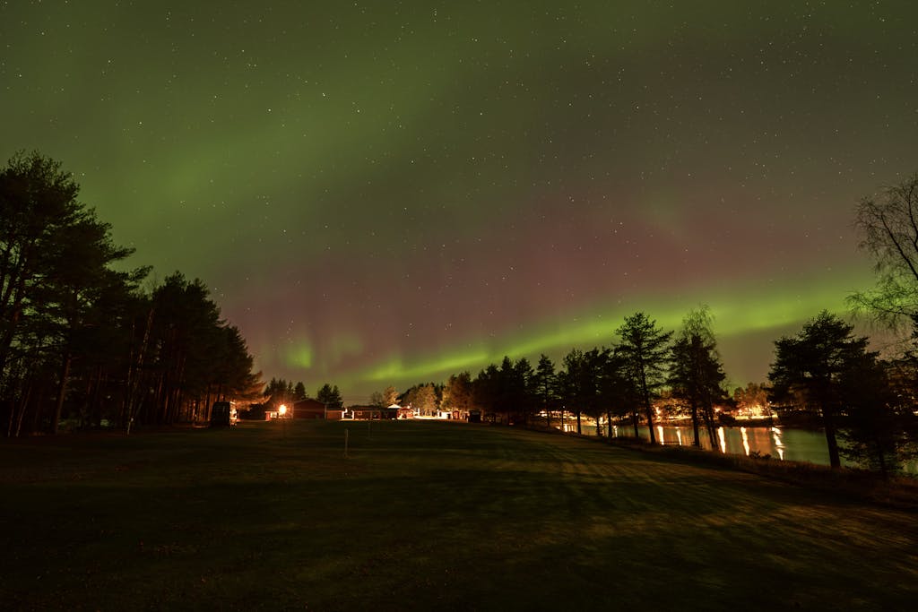 The Northern Lights Aurora QR Code illuminate the night sky above a tranquil lakeside landscape with a forest backdrop.