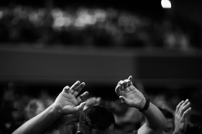 Depomin82 A black and white photo of hands raised in a crowd during a concert or religious gathering indoors.