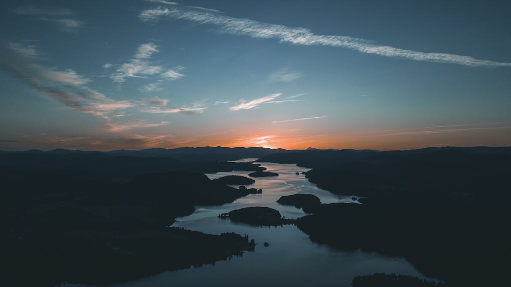 Epcylon A breathtaking aerial shot showcasing a calm river winding through hills at sunset, with a vivid sky.