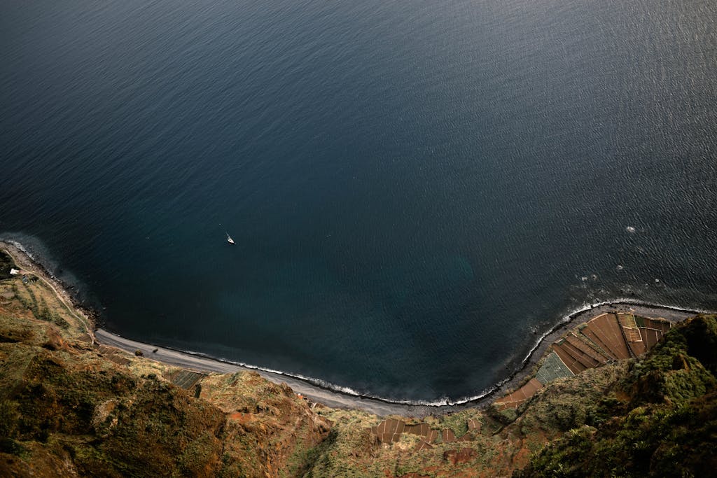 Nikane Madeira A breathtaking aerial view of Madeira's coastline and ocean with a lone sailboat.