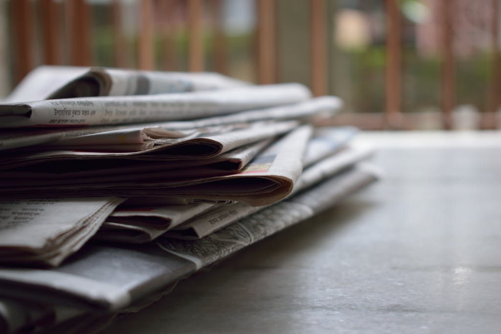 Newstoday Newsgiga A close-up of a stack of newspapers resting on a desk, symbolizing information and media.