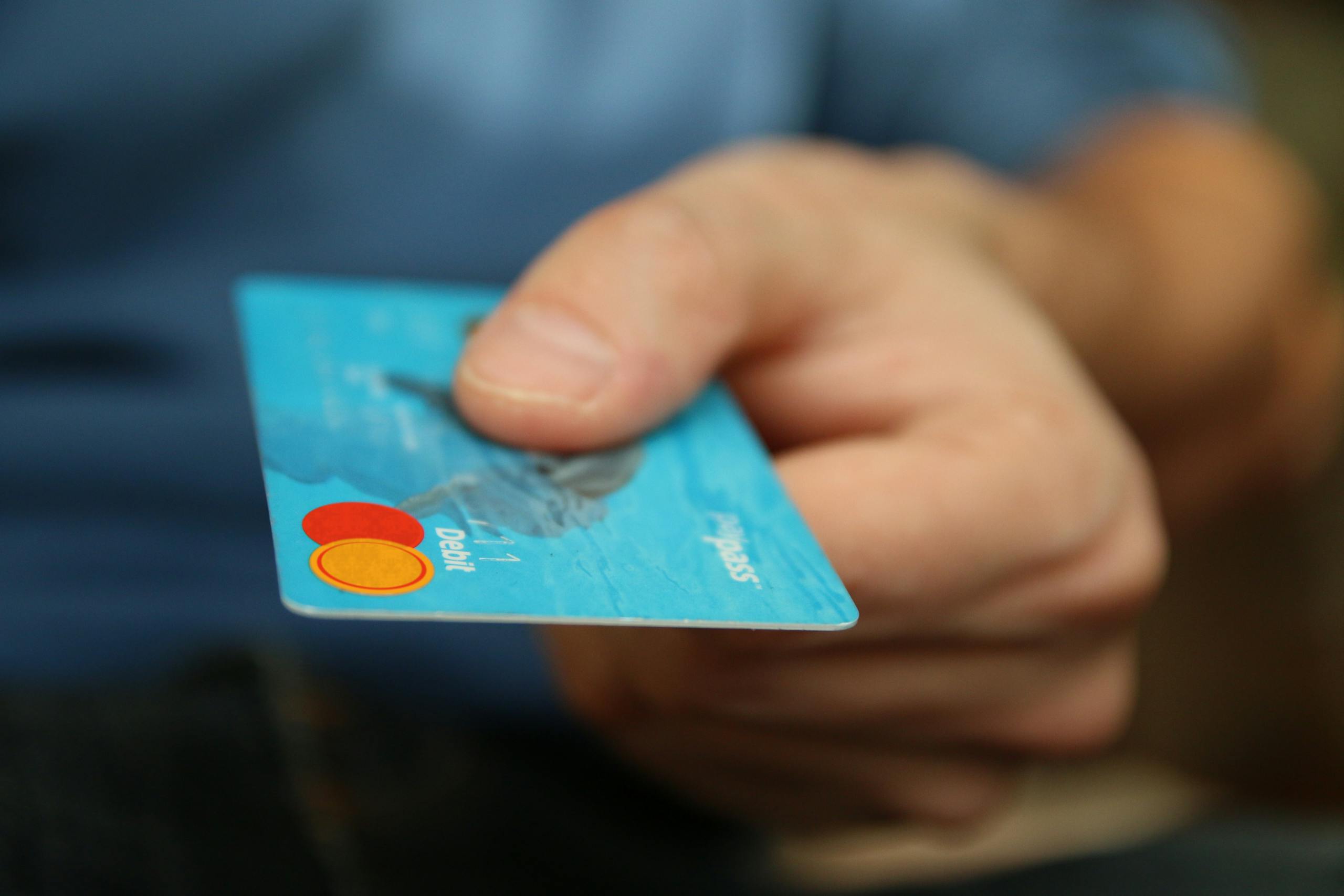 Magento Service Gonzay A close-up shot of a hand offering a blue debit card for payment.