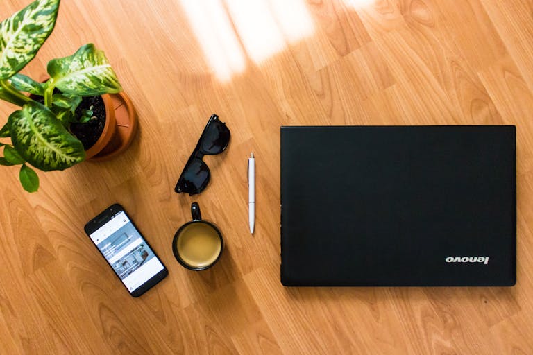 i Square – Lenovo Ex A flat lay of a desk with a laptop, coffee cup, smartphone, and plant, perfect for a modern office setting.