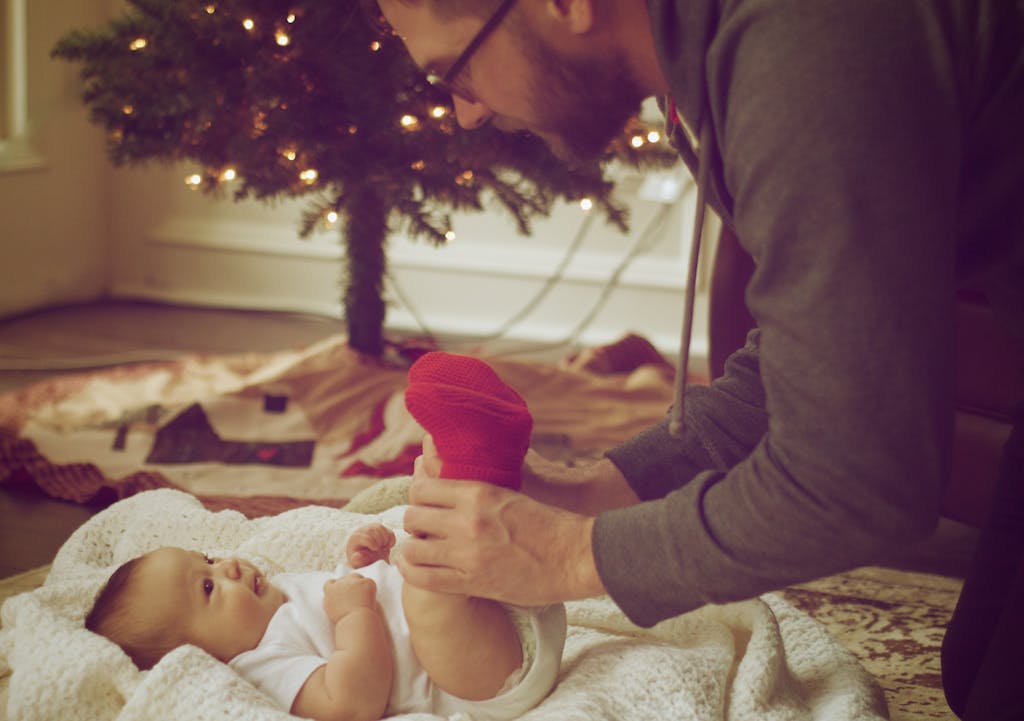 Sodiceram A loving father plays with his newborn near a festive Christmas tree indoors.