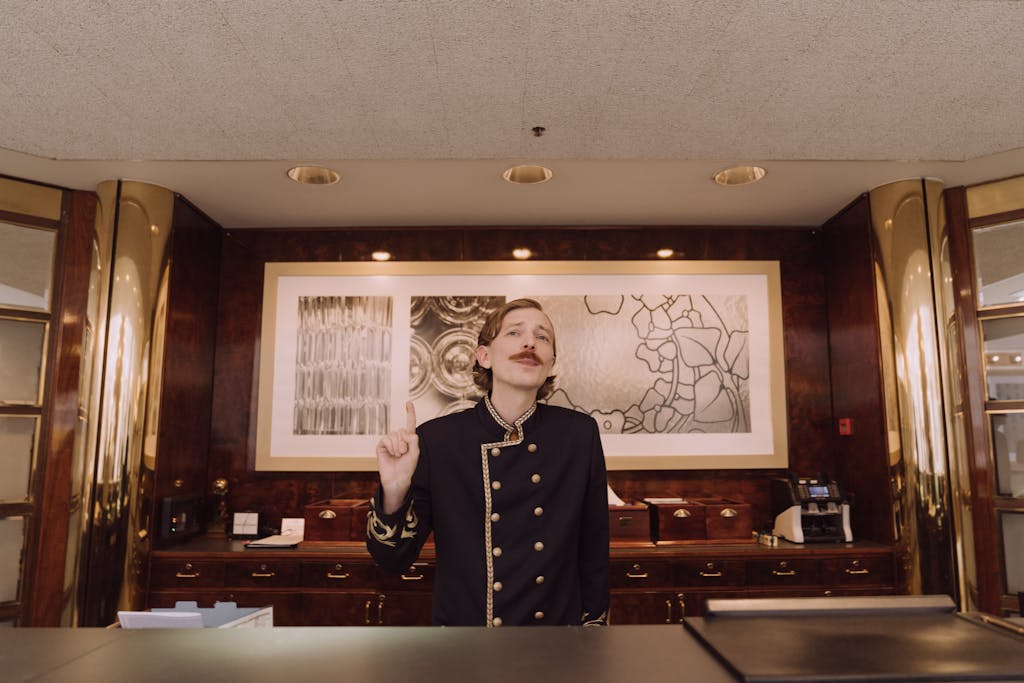 Magento Service Gonzay A luxury hotel receptionist in uniform stands behind the opulent front desk, ready to assist guests.