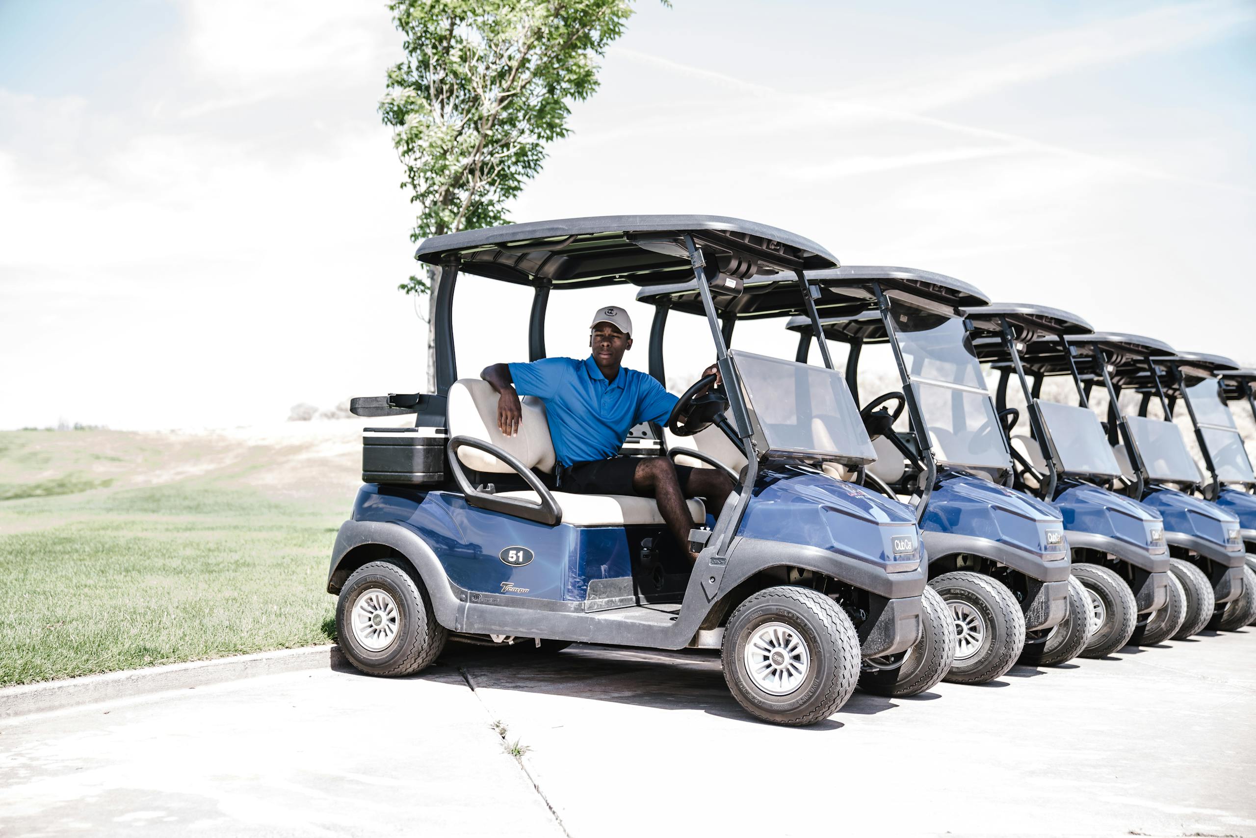 Golf Cart Seat Covers A man sitting in a row of blue golf carts parked on a sunny day.