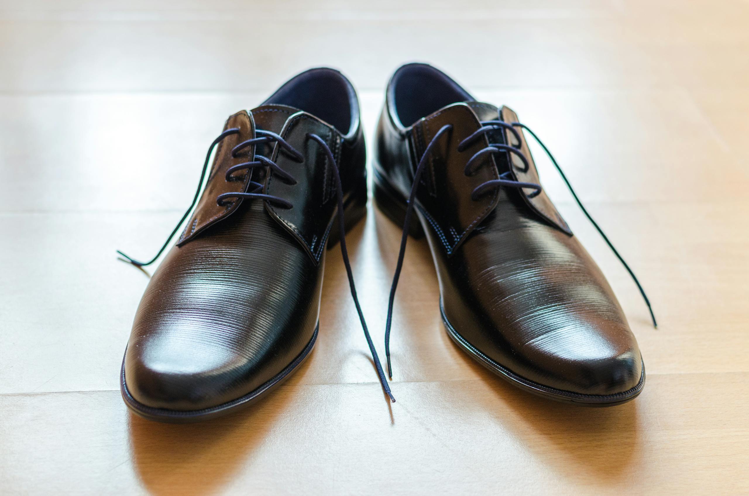 Kidlings Shoes A pair of shiny, elegant black leather dress shoes with laces on a wooden floor.