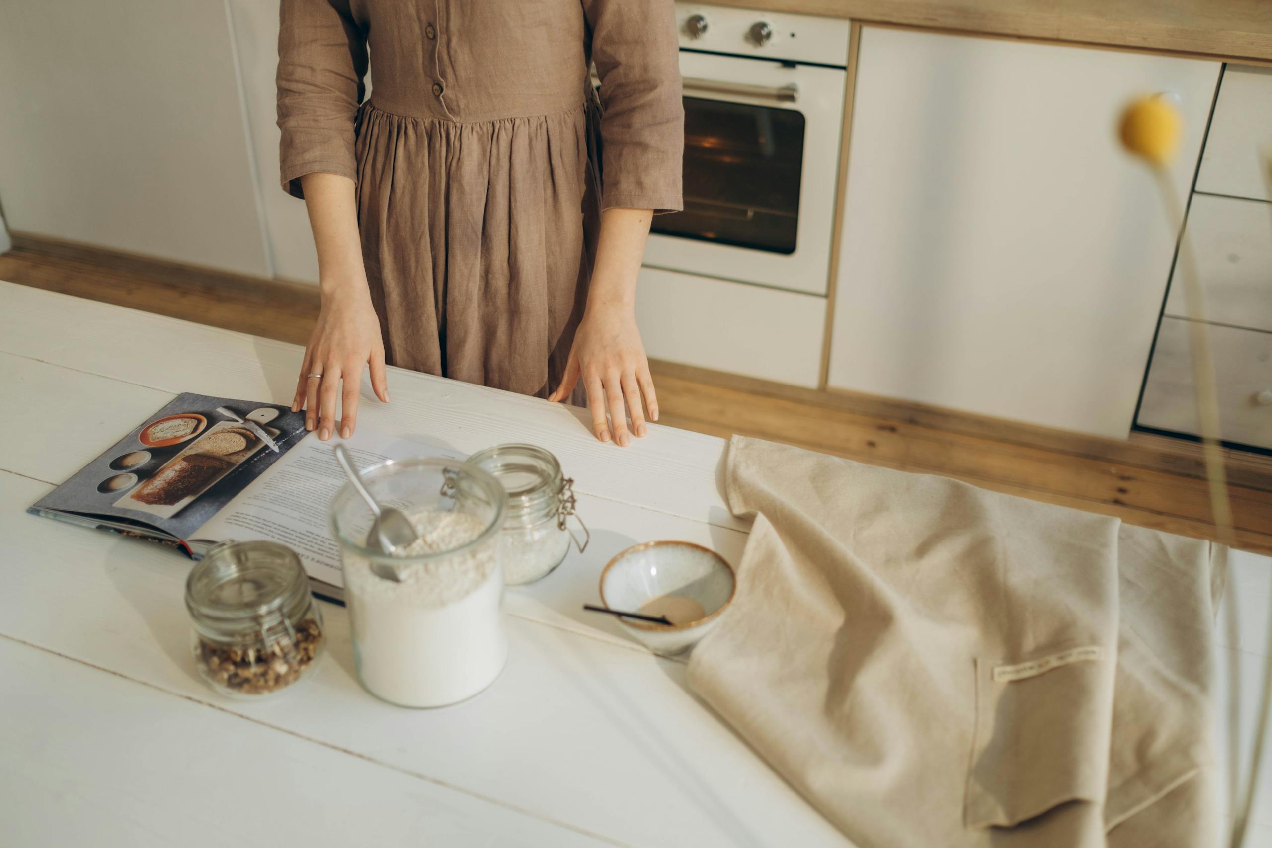 Recipeasy Recipes A person prepares ingredients on a wooden kitchen table with a cookbook for baking.