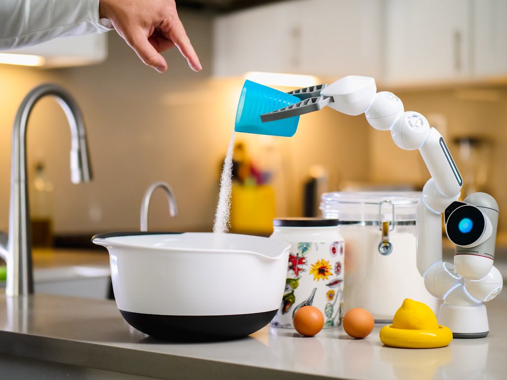 Auztron Bot A robot arm assists in baking by pouring ingredients into a mixing bowl in a modern kitchen.