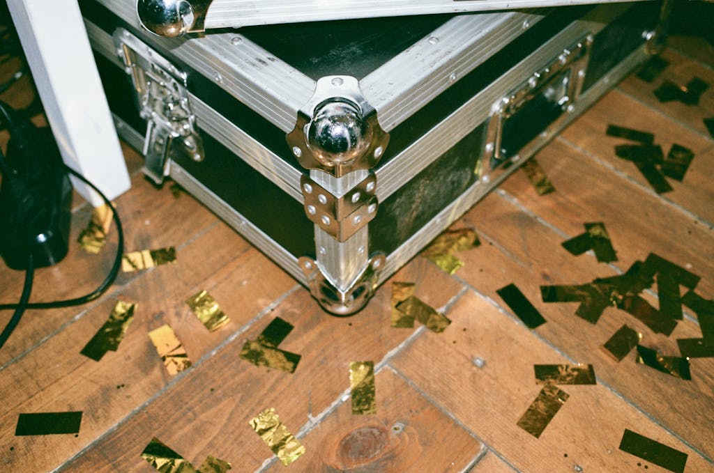 Simbramento A vintage metal trunk surrounded by gold confetti pieces on a rustic wooden floor indoors.