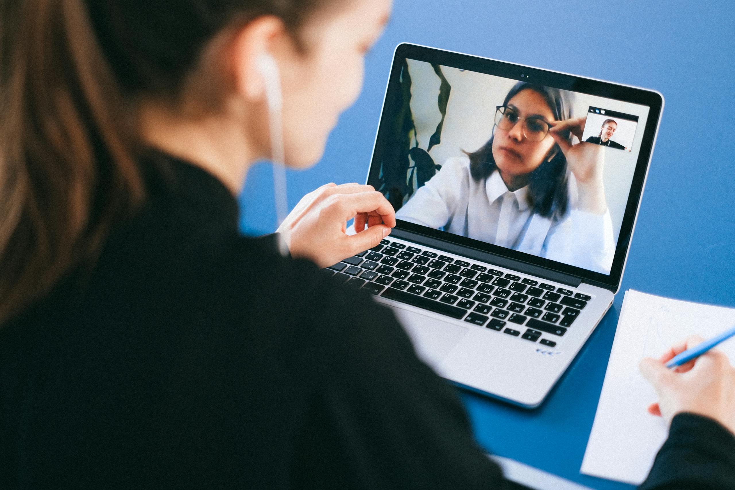 Virtual Meeting A woman engaged in a video conference call, taking notes during a professional meeting.