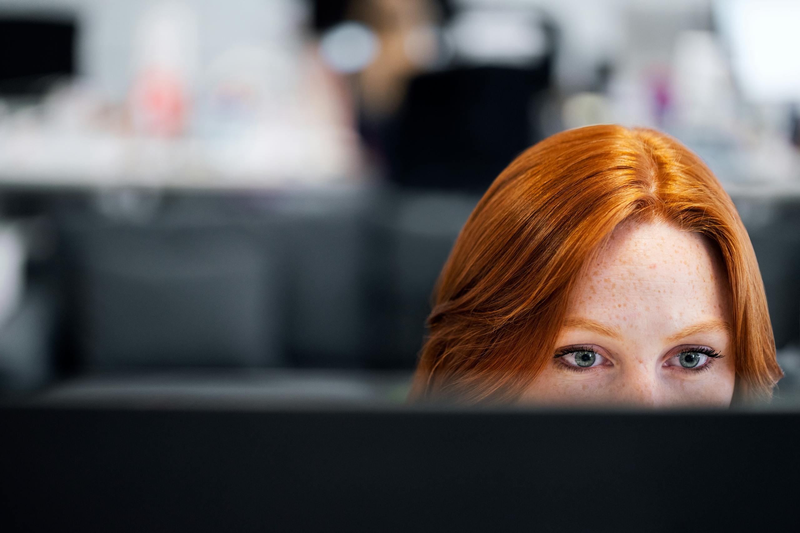 Employee Scheduling Software A woman with red hair intensely focused on a computer screen in an office setting.
