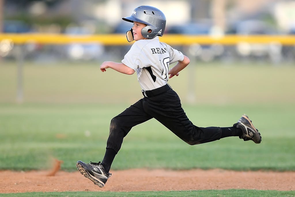 Runlia Action shot of a young baseball player running fast on the field, wearing uniform and helmet.