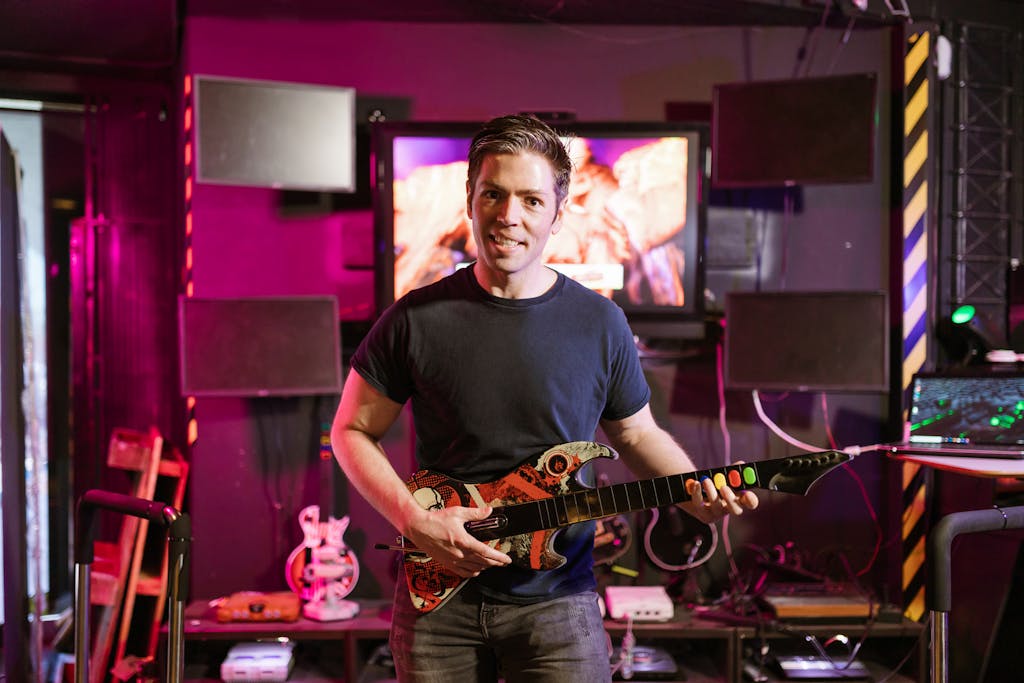 Xbocmy Adult male playing guitar controller in a vibrant gaming setup indoors, showcasing esports and recreation.