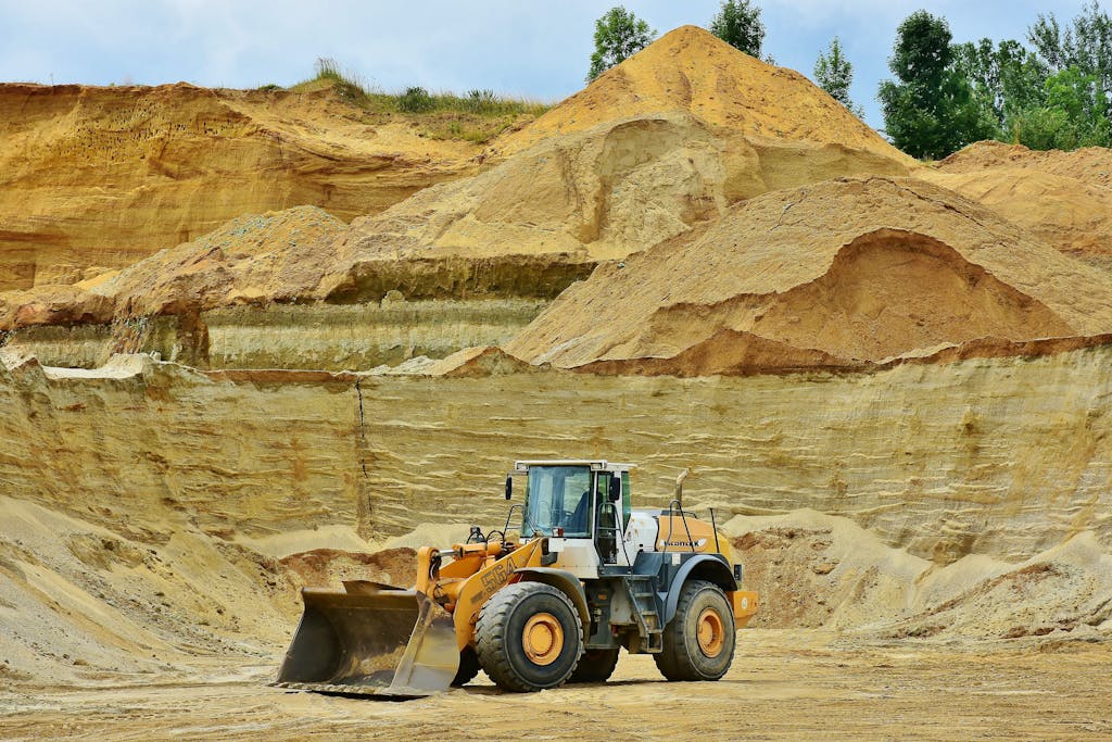 Buscrs An excavator working in an open pit mine surrounded by sandy terrain and clear sky.