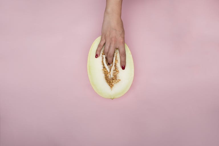 Simbramento Artistic expression with hand touching a melon, resembling modern conceptual symbolism on a pink backdrop.