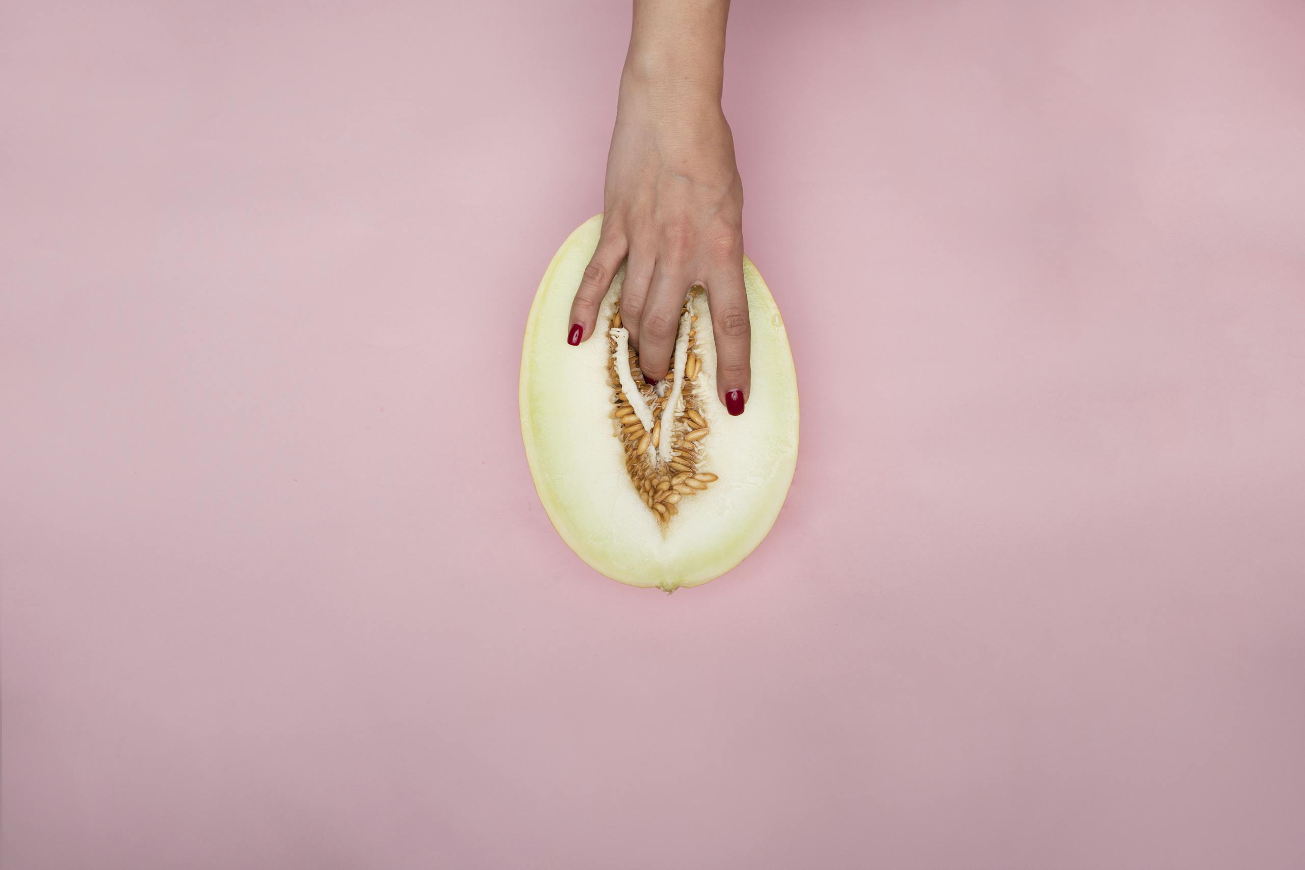 Simbramento Artistic expression with hand touching a melon, resembling modern conceptual symbolism on a pink backdrop.
