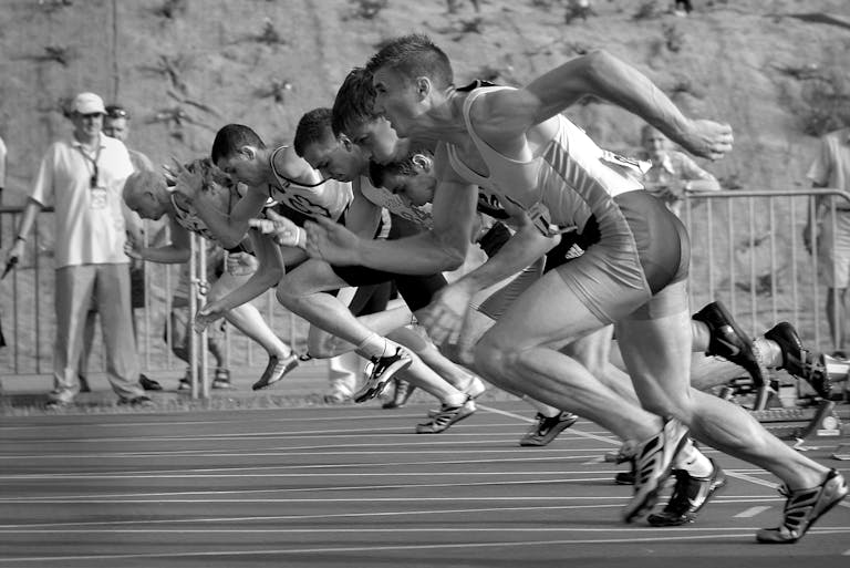 Runlia Athletes burst from the blocks during a sprint race, captured in monochrome.
