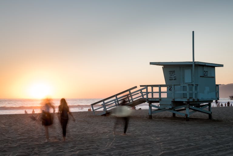 Monika Leveski Beach scene at sunset with a lifeguard tower and people in motion at Santa Monica, CA.