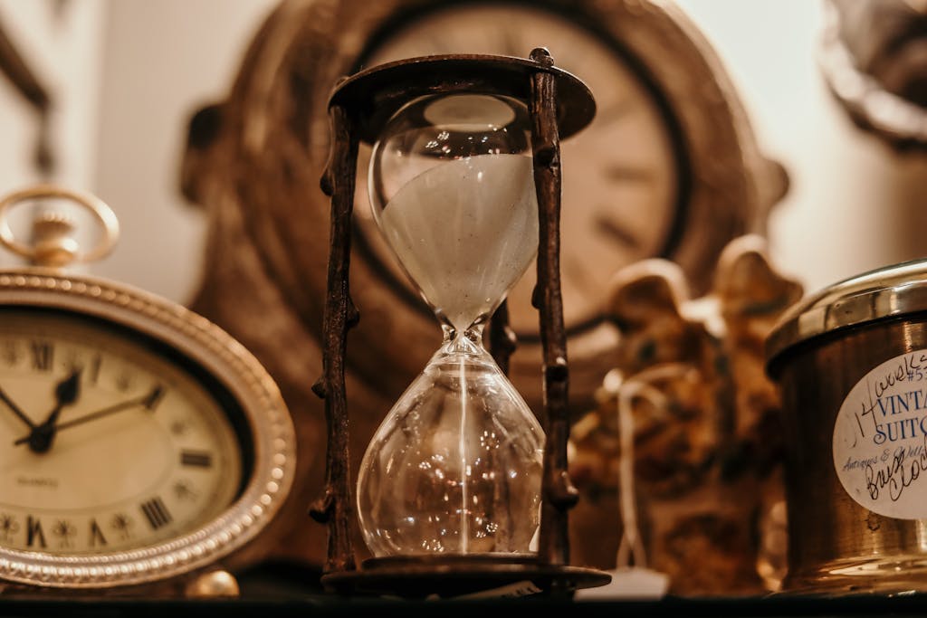 TimesNowNews Close-up of a vintage hourglass surrounded by antique clocks in warm lighting.