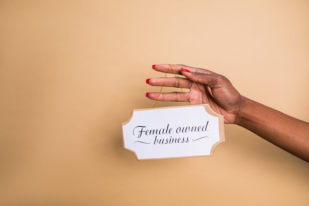 Xson208 Close-up of a woman's hand holding a 'Female Owned Business' sign on a beige background.