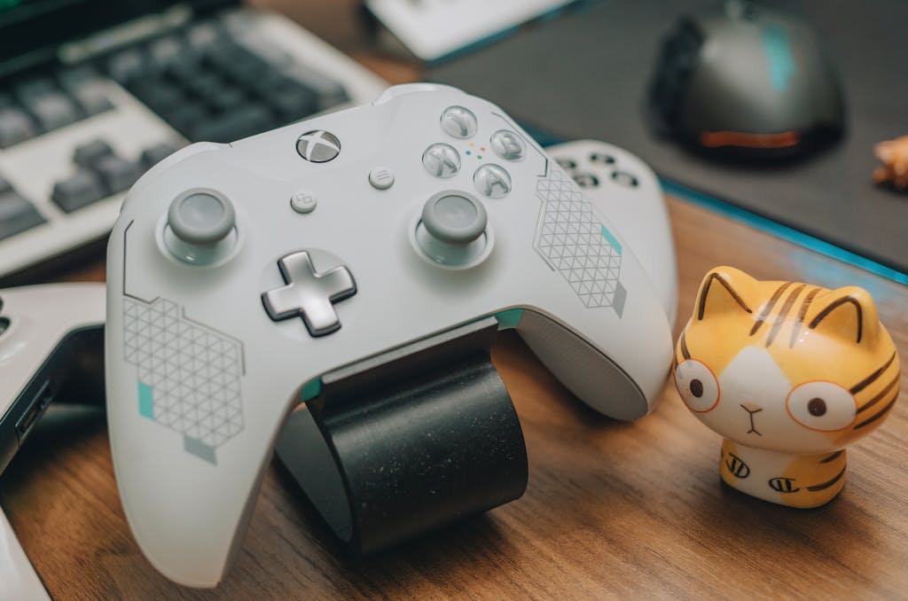 Xbocmy Close-up of an Xbox game controller with a toy, mouse, and keyboard on a desk, showcasing a gaming setup.