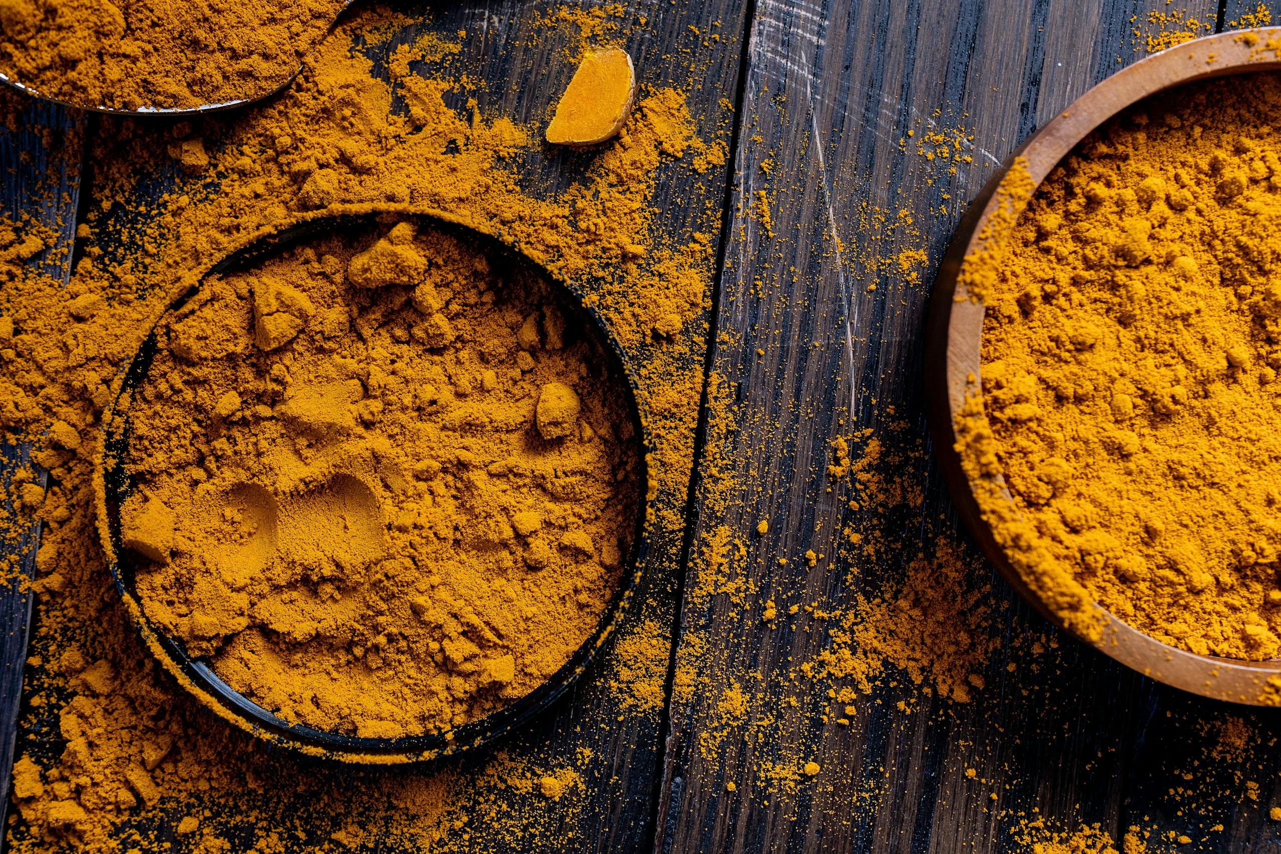 Well Health Organic Ayurveda Close-up of turmeric powder in rustic bowls on a wooden surface, ideal for spice and food photography.