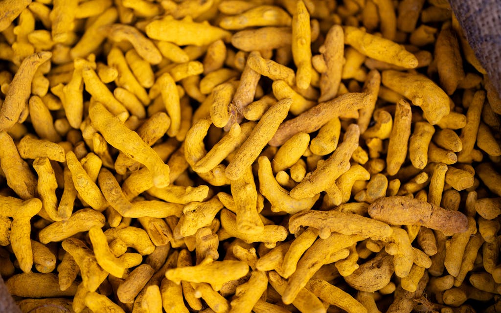 Well Health Organic Ayurveda Detailed view of turmeric roots in a market setting, showcasing their vivid yellow color.