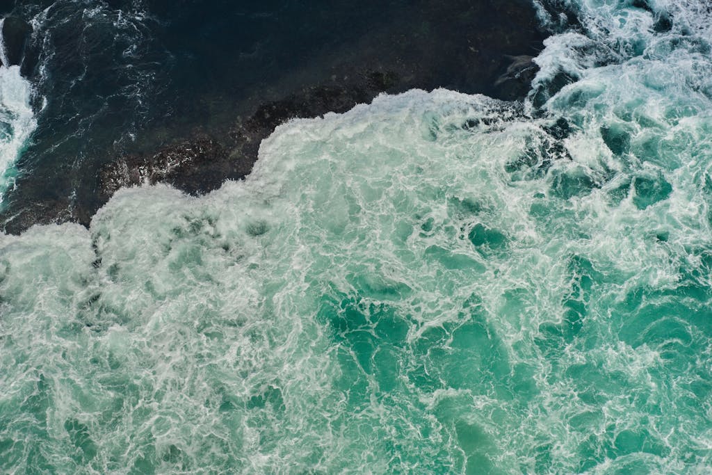 Naruto Senki Dynamic aerial view of turquoise waves crashing on rocky coast in Naruto, Japan.