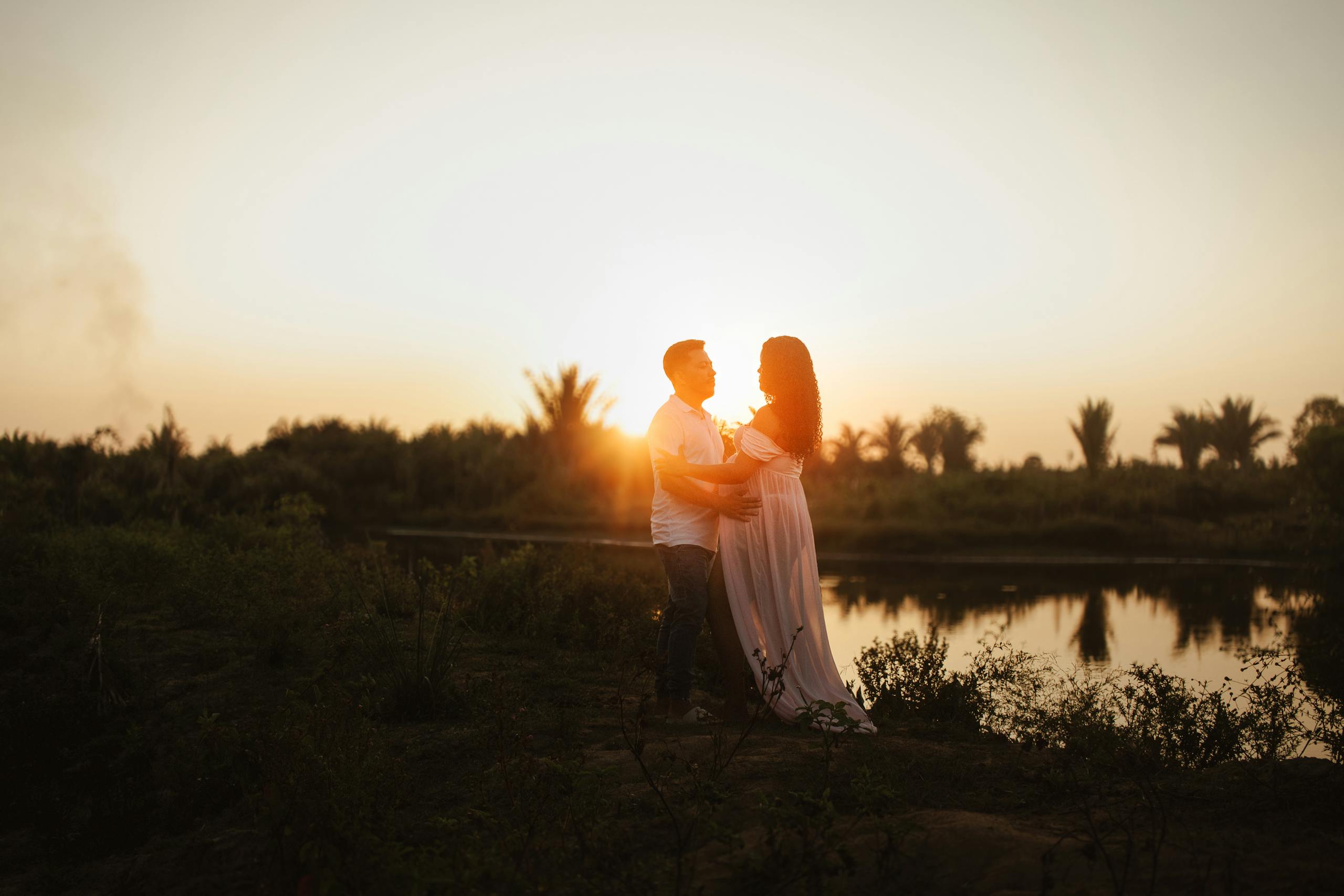 Naruto Senki Expecting couple embraces by a serene river at sunset, symbolizing love and new beginnings.