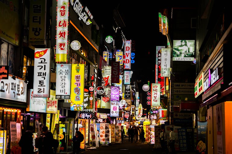 Koriandri Explore Seoul's vibrant nightlife on a bustling neon-lit street lined with shops and restaurants.