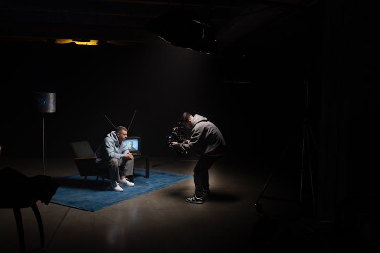 Film productionshoot Mozarabic Hoodie indoors with cinematographer filming an actor sitting, studio lighting.