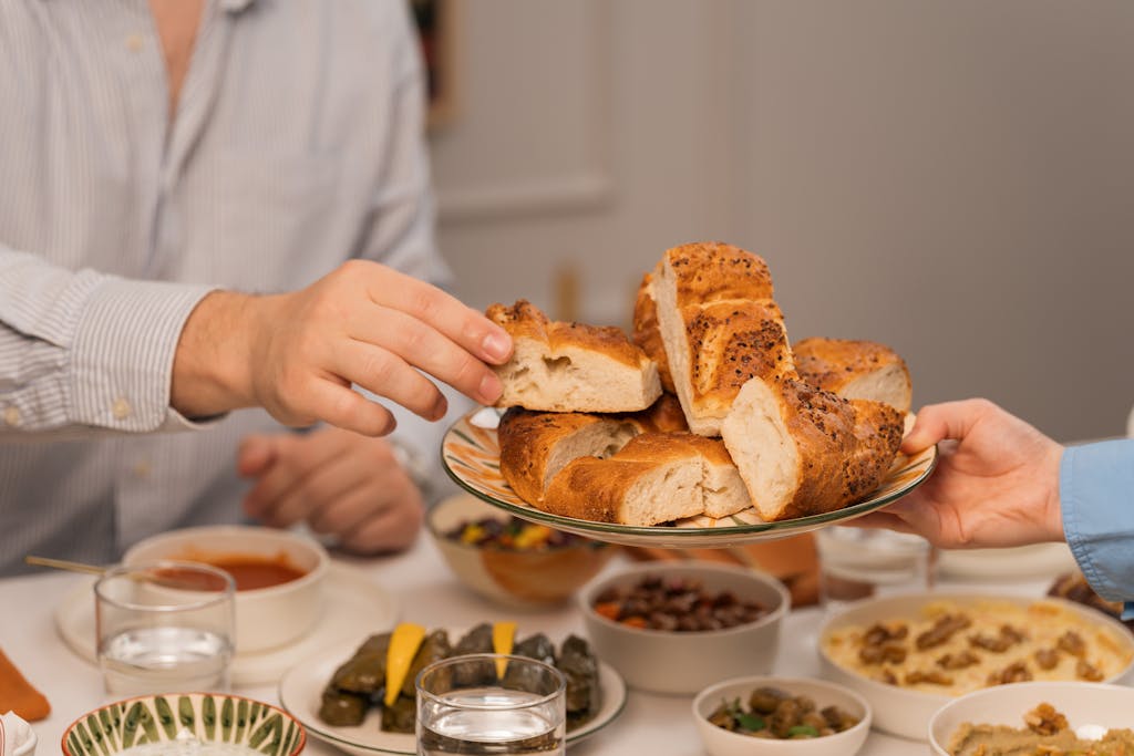Recipeasy Recipes Hands exchanging fresh bread at a dinner table filled with diverse dishes and drinks.