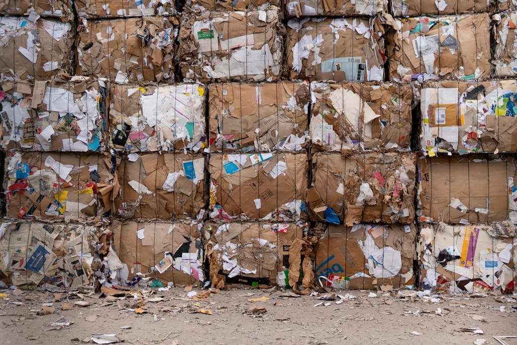 Uyç Large bales of recycled cardboard stacked outdoors, ready for processing.