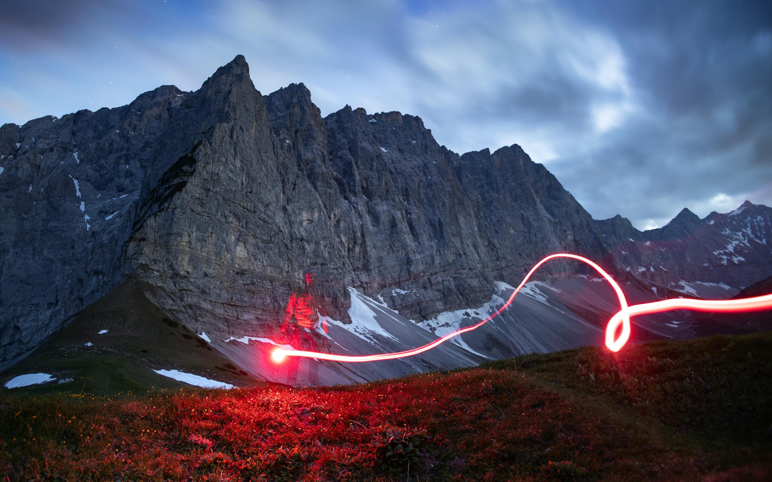 Robert Golob Mysterious alpine mountain scene with striking red light trail at dusk.