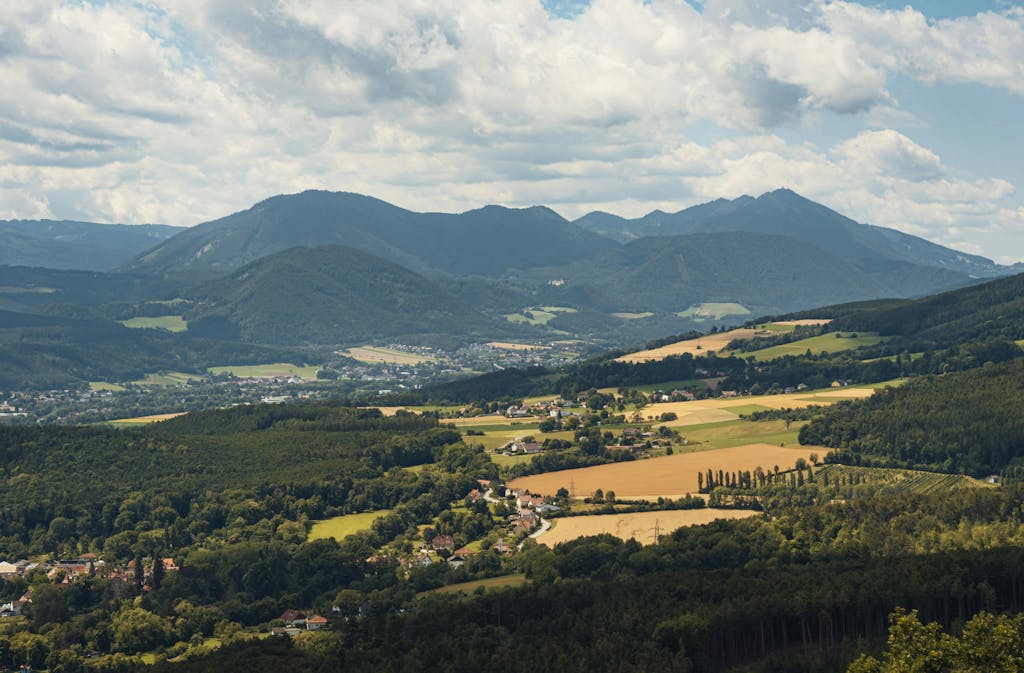 Impupdates.comwow Independence Panoramic view of Ternitz, Austria showcasing rolling hills and expansive mountain ranges under a cloudy sky.