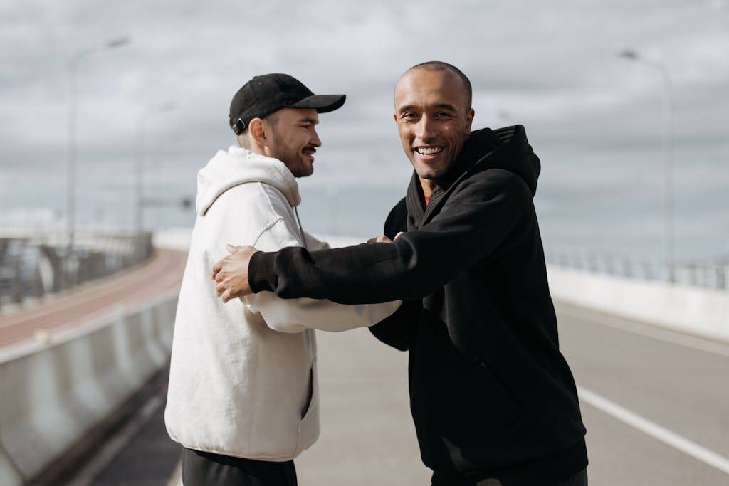 Mozarabic Hoodie Two friends smiling and embracing on a sunny day outdoors on a road.