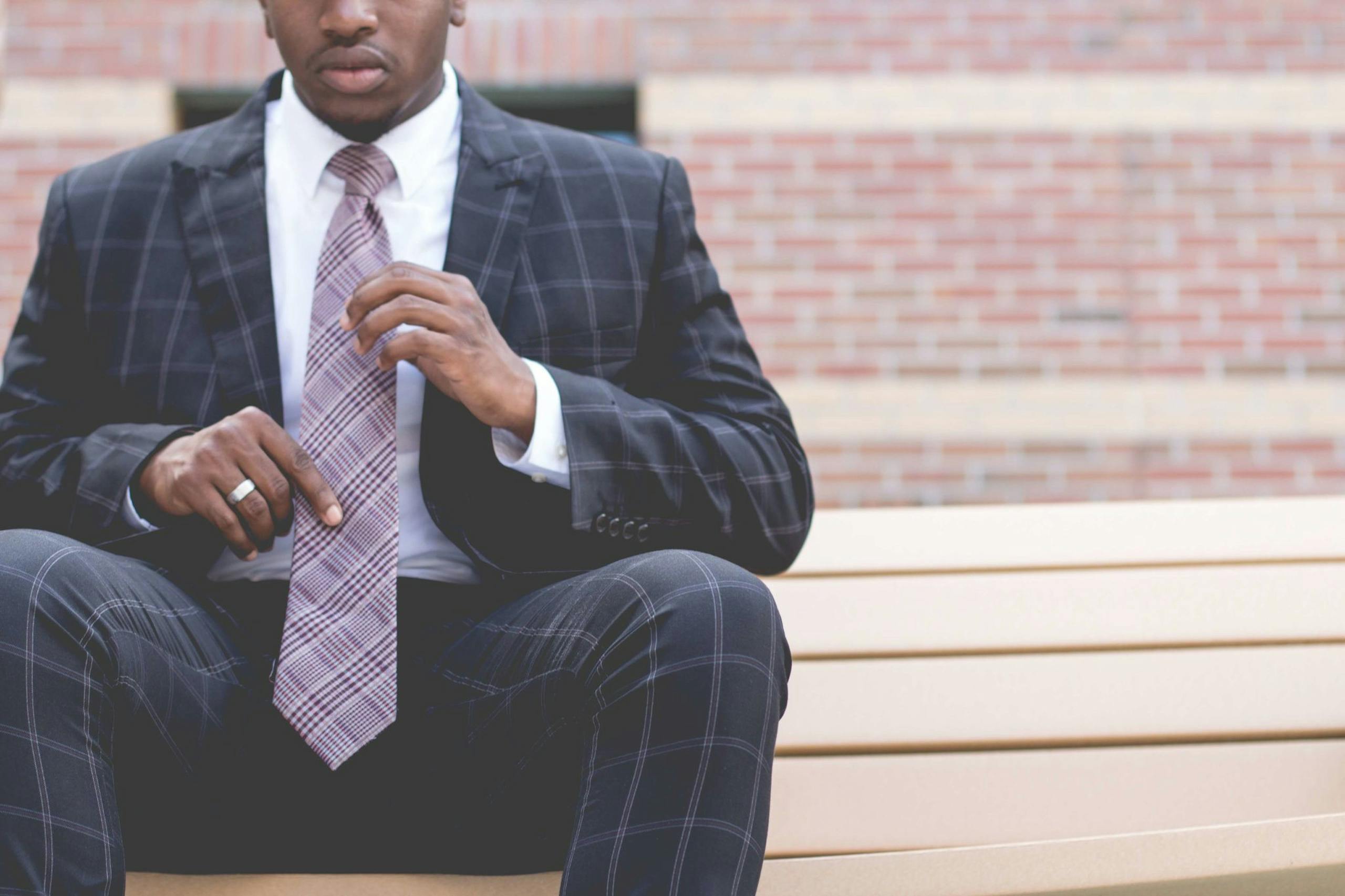 Blazertje A confident, professional man adjusts his tie while sitting outdoors, showcasing style and poise.